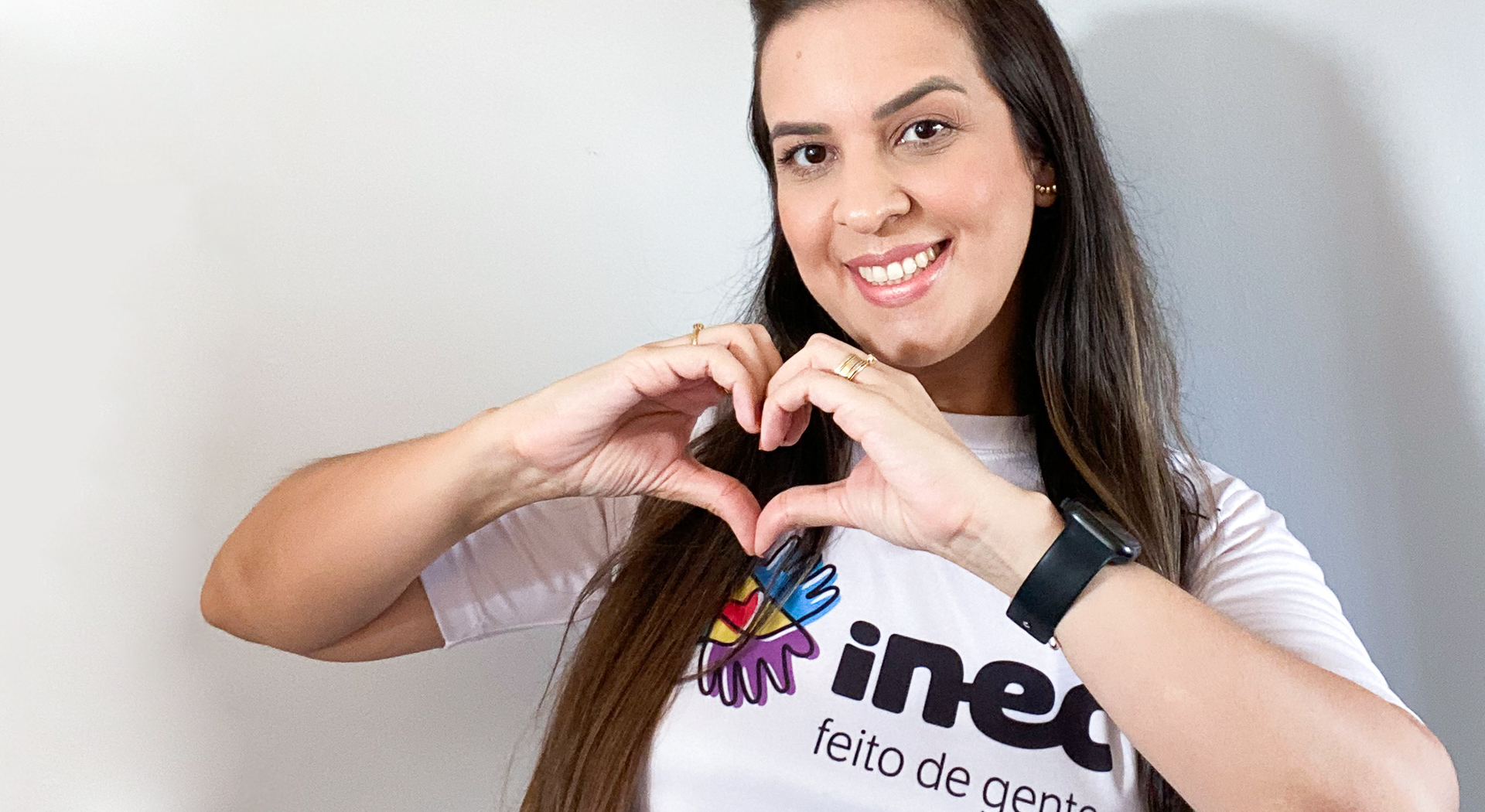 Mulher com a blusa do Inec fazendo o sinal do coração com as mãos.