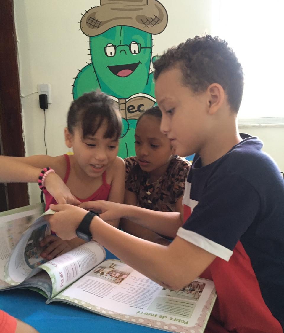 Três crianças folheando um livro no espaço de leitura ballet raio de sol depois da revitalização