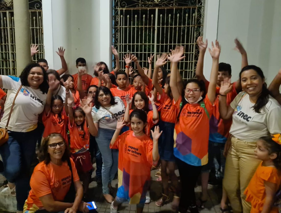 A imagem mostra algumas crianças na frente do letreiro do Theatro José de Alencar reunidas usando a camisa do projeto Espaço de Leitura