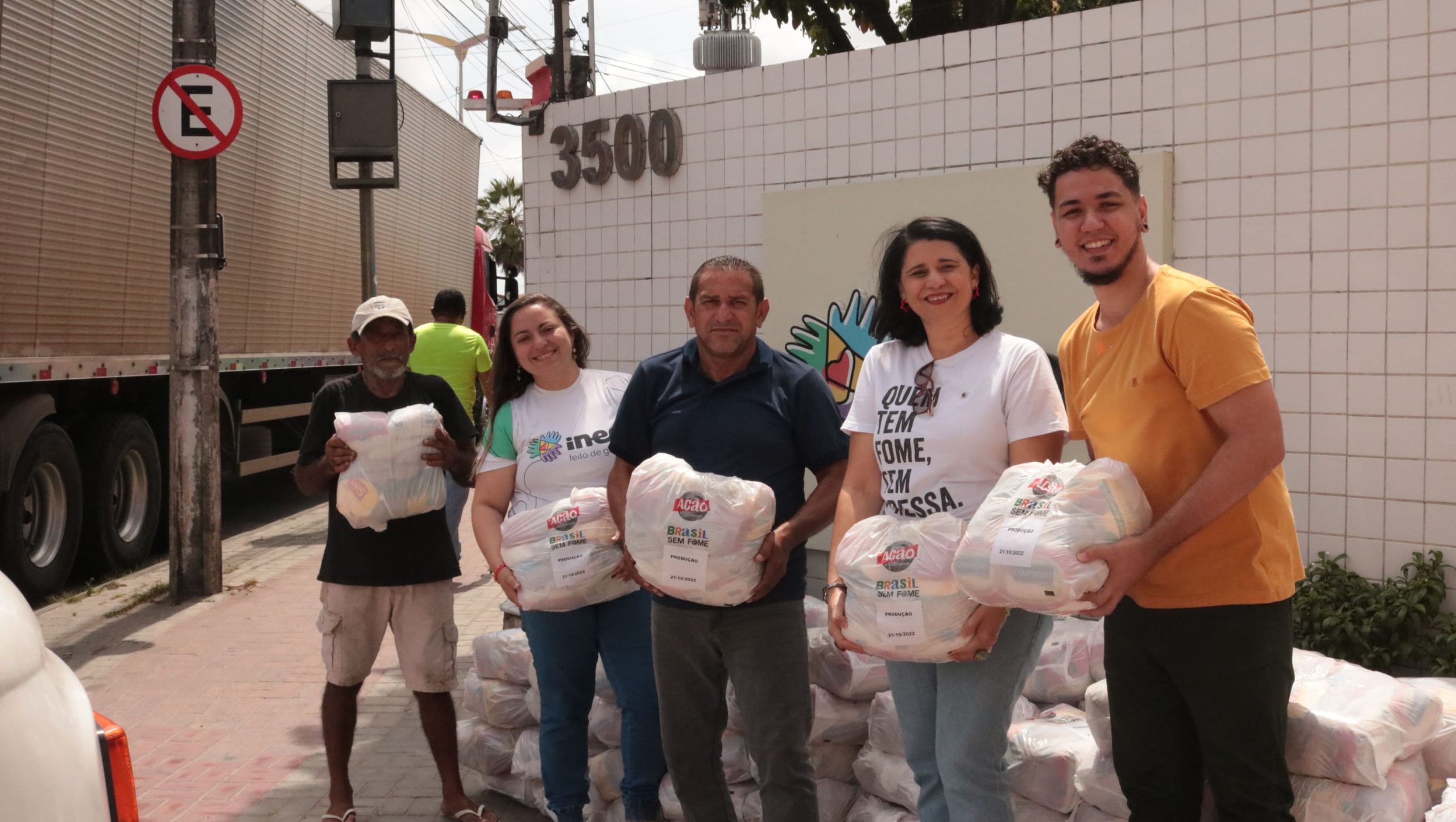 A imagem mostra cinco pessoas, cada uma delas segurando uma cesta básica com a logo da Ação da Cidadania. As cestas fazem parte da campanha natal sem fome 2022