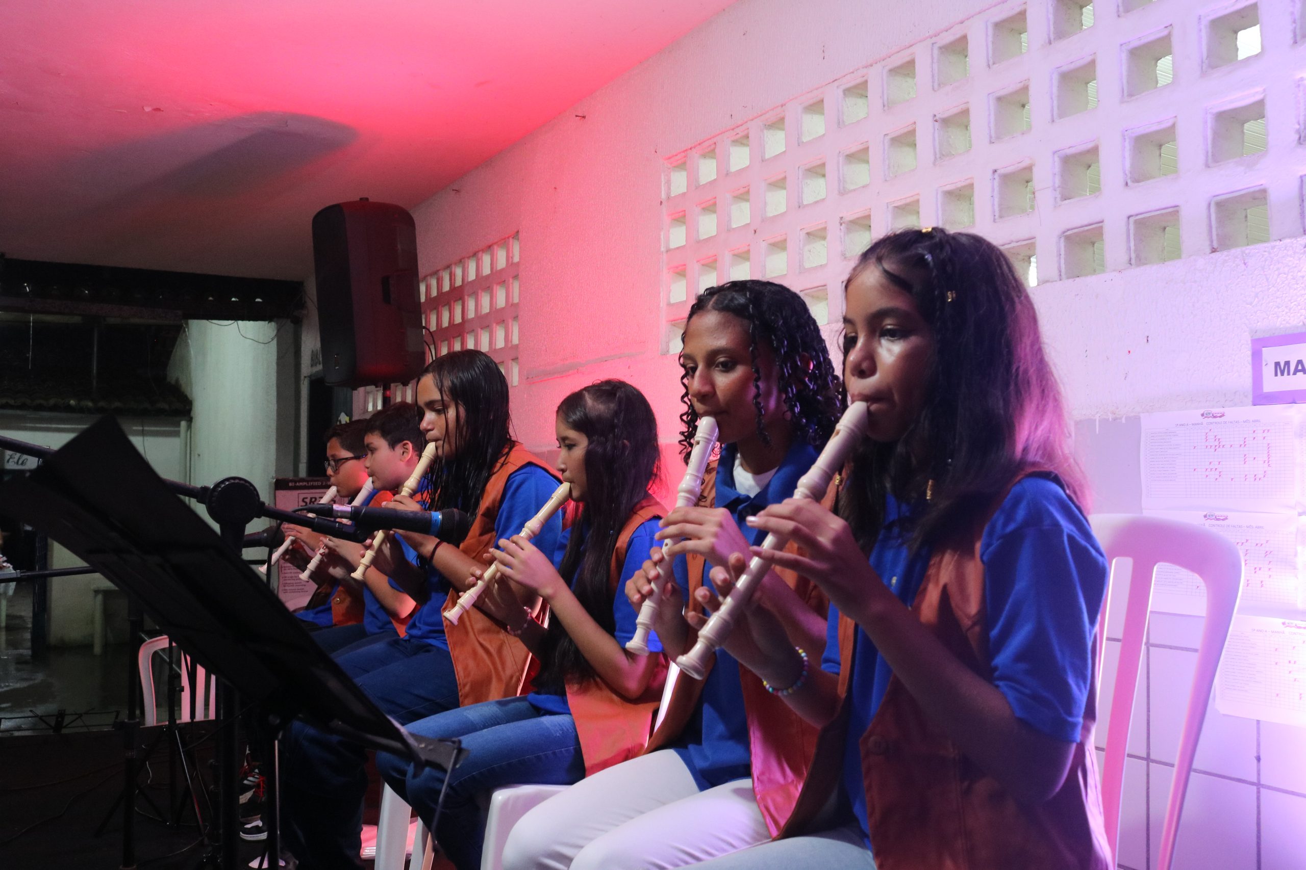 Na foto vemos crianças de todas as idades, vestindo uma blusa azul e tocando flauta.