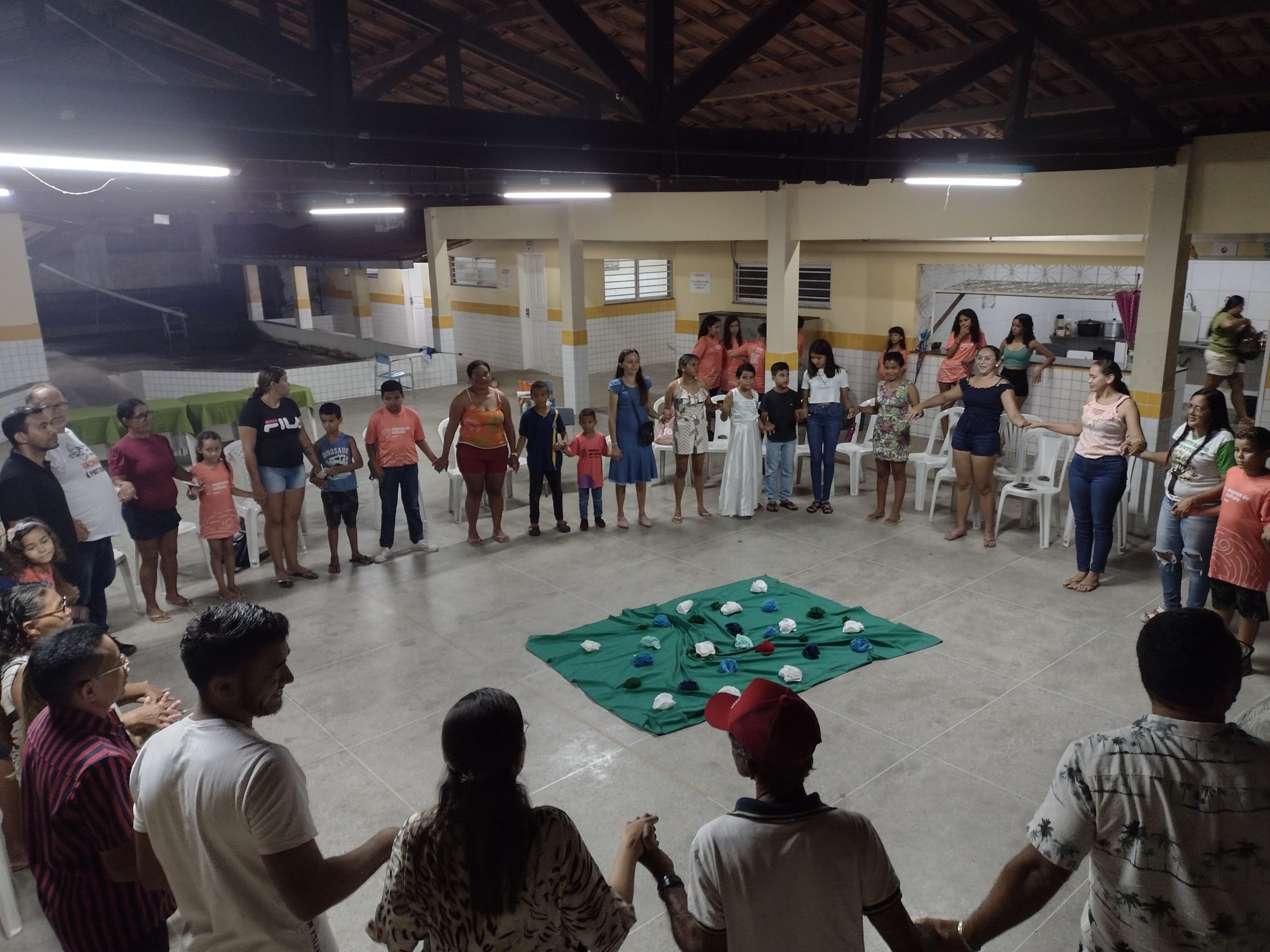 Pessoas de diversas idades em uma escola reunidas em uma roda a noite com