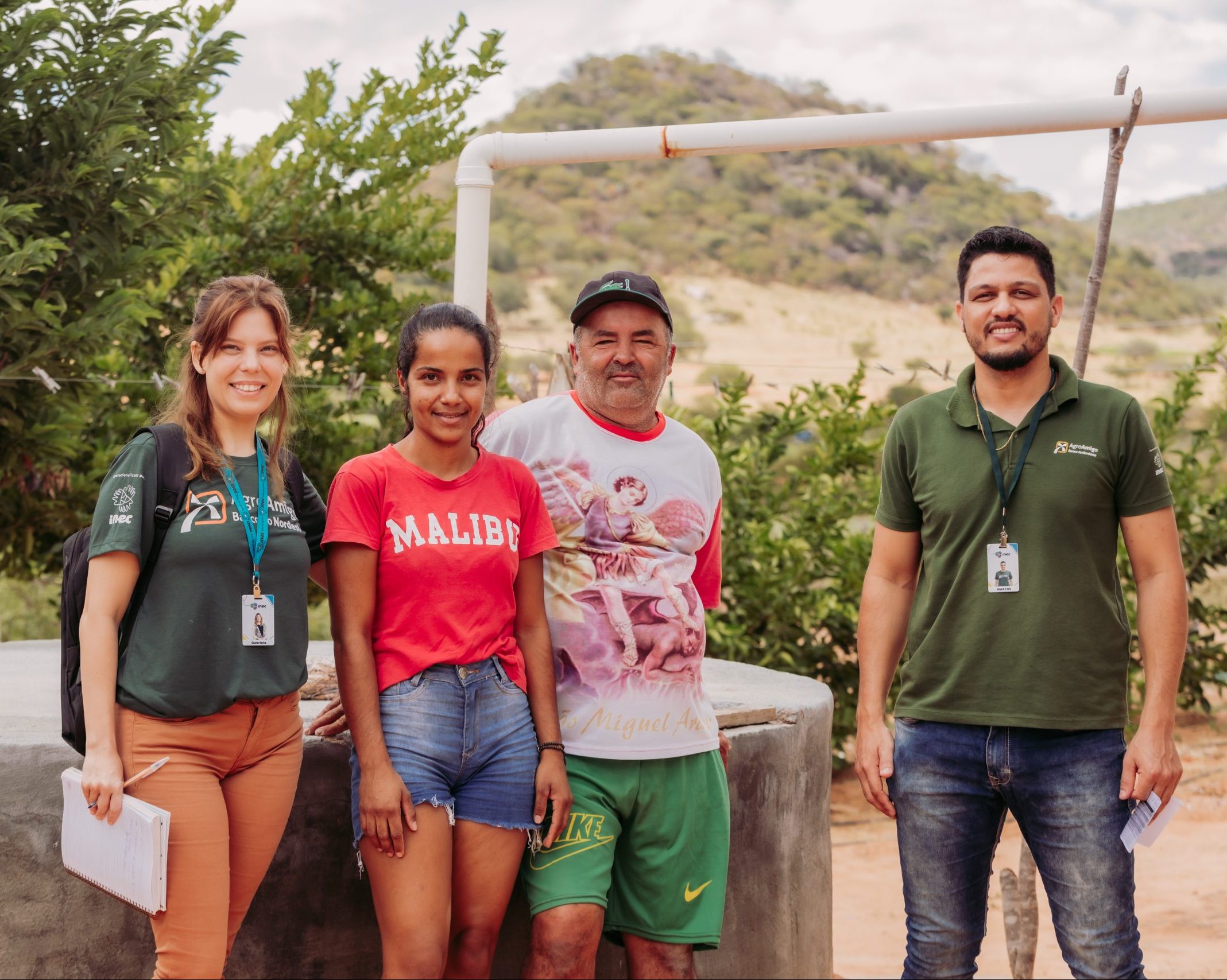 Na imagem vemos dois agentes com a camisa verde do agro e dois clientes encostados numa cisterna