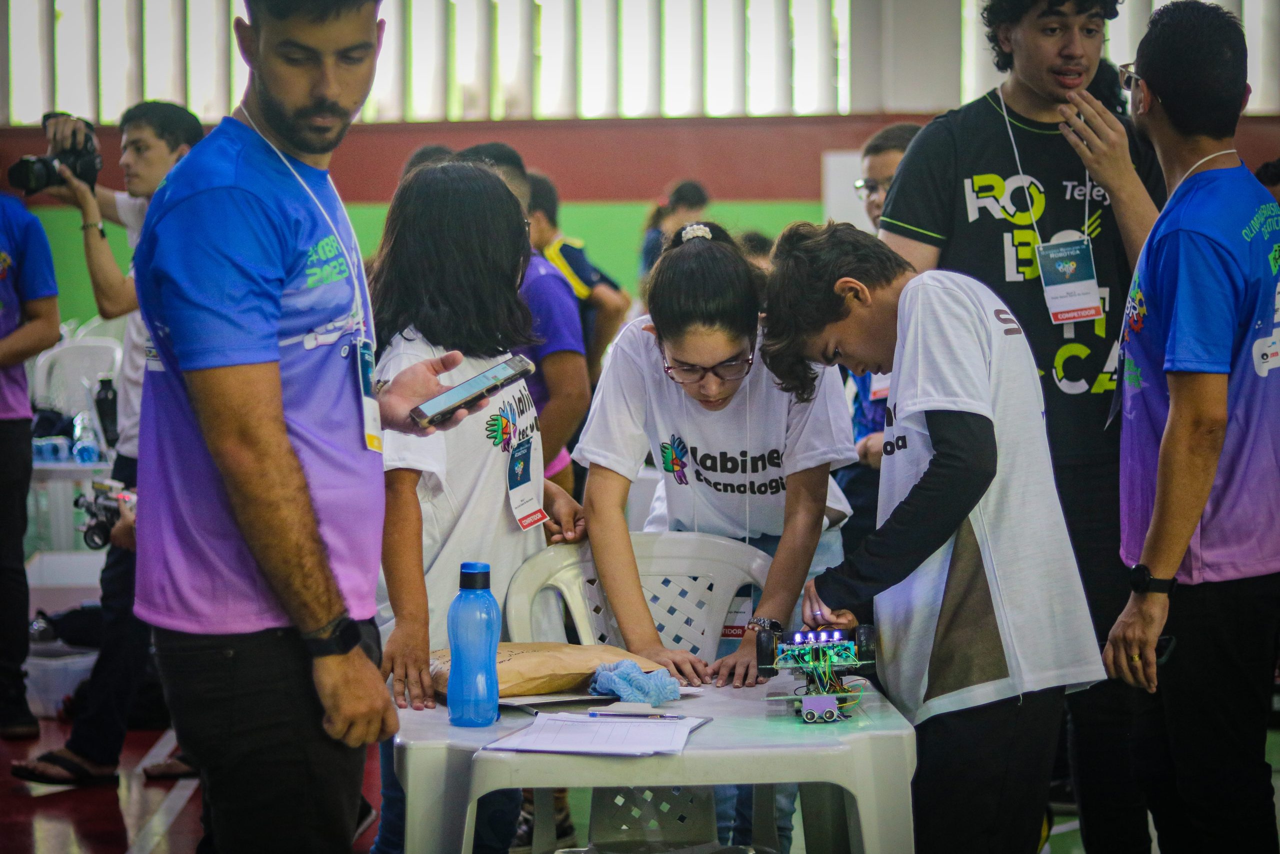 A imagem mostra a equipe start ligando o robô, ao lado um assistente da OBR acompanha a equipe