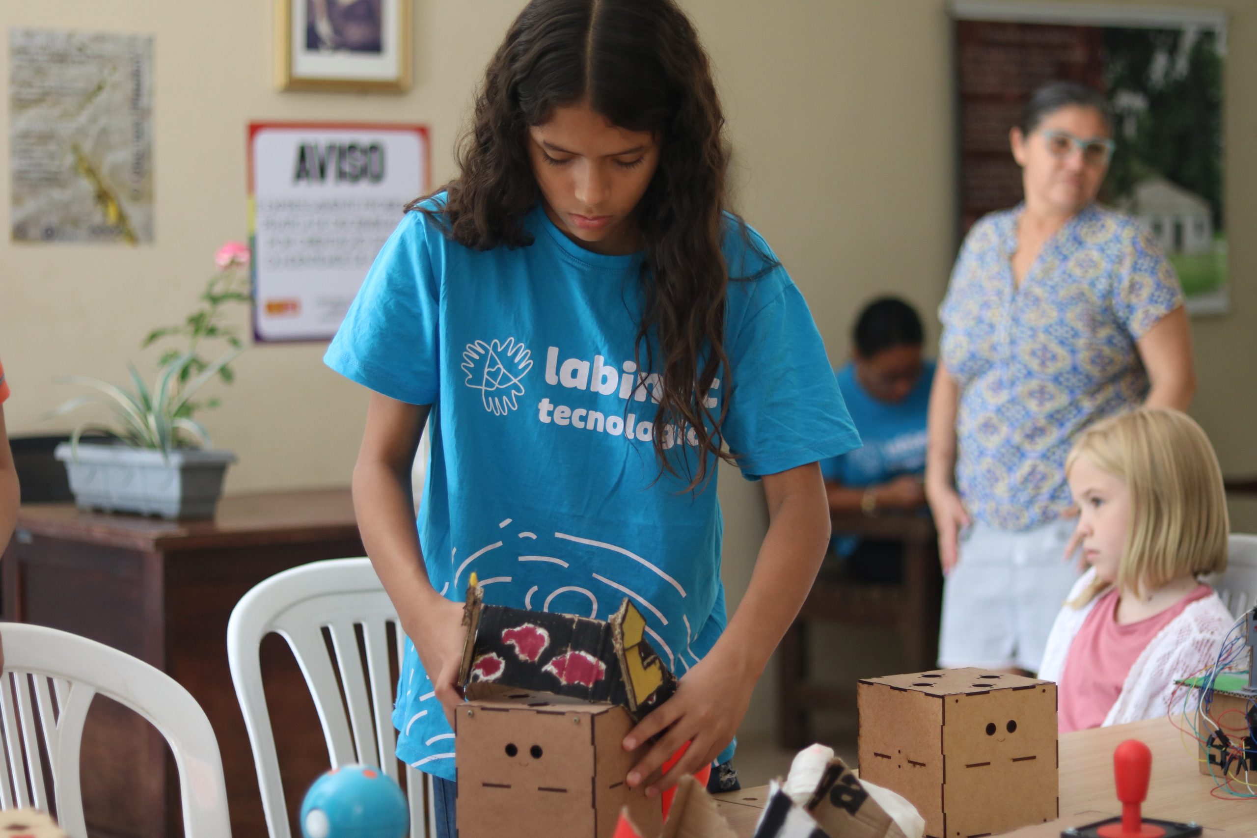 Na imagem uma aluna do Labinec Vila União segura um dos robôs expostos, na Feira do Zé. A garota está vestida com uma blusa azul