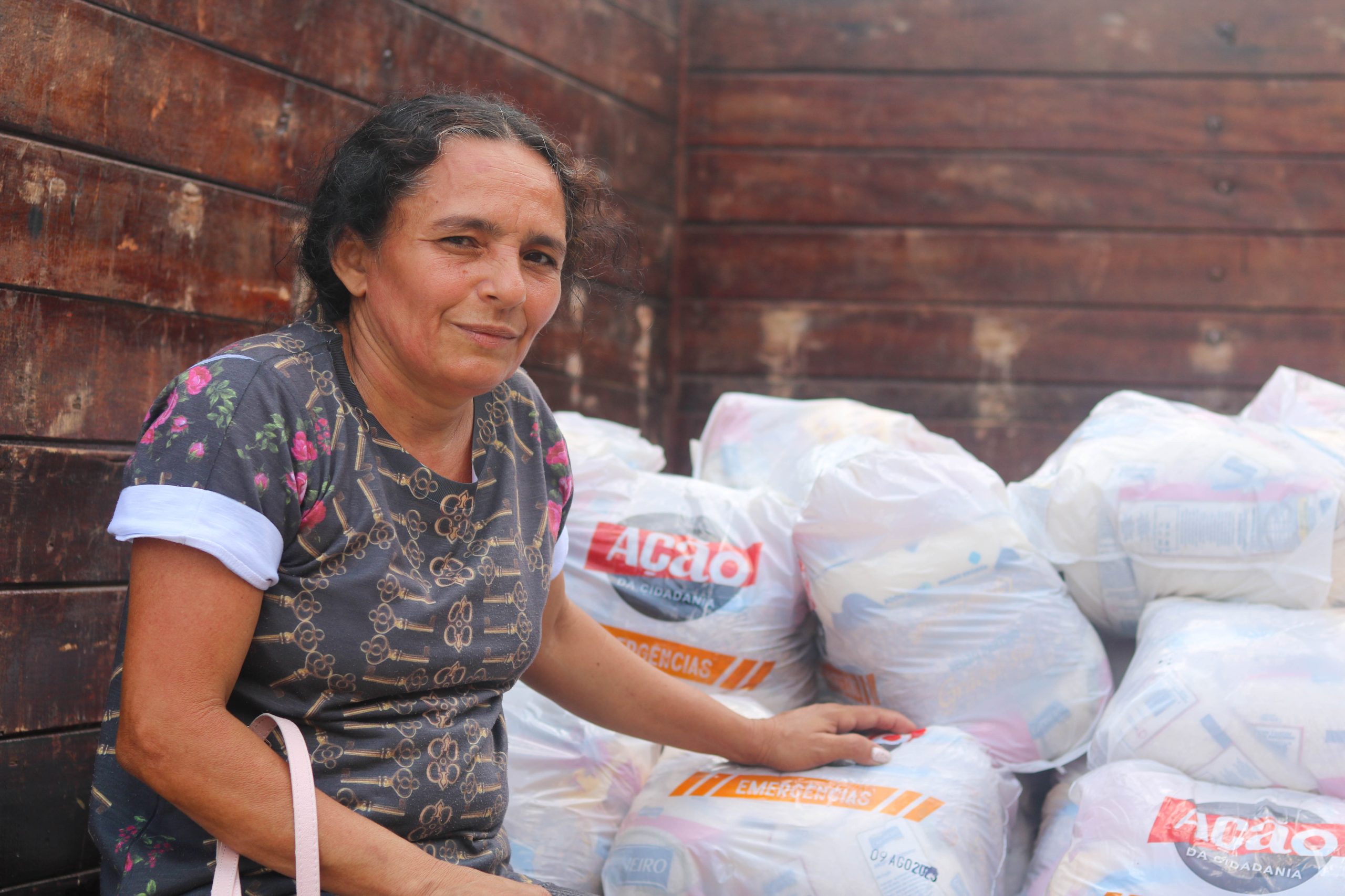 senhora posa ao lado de cestas da campanha natal sem fome 2023