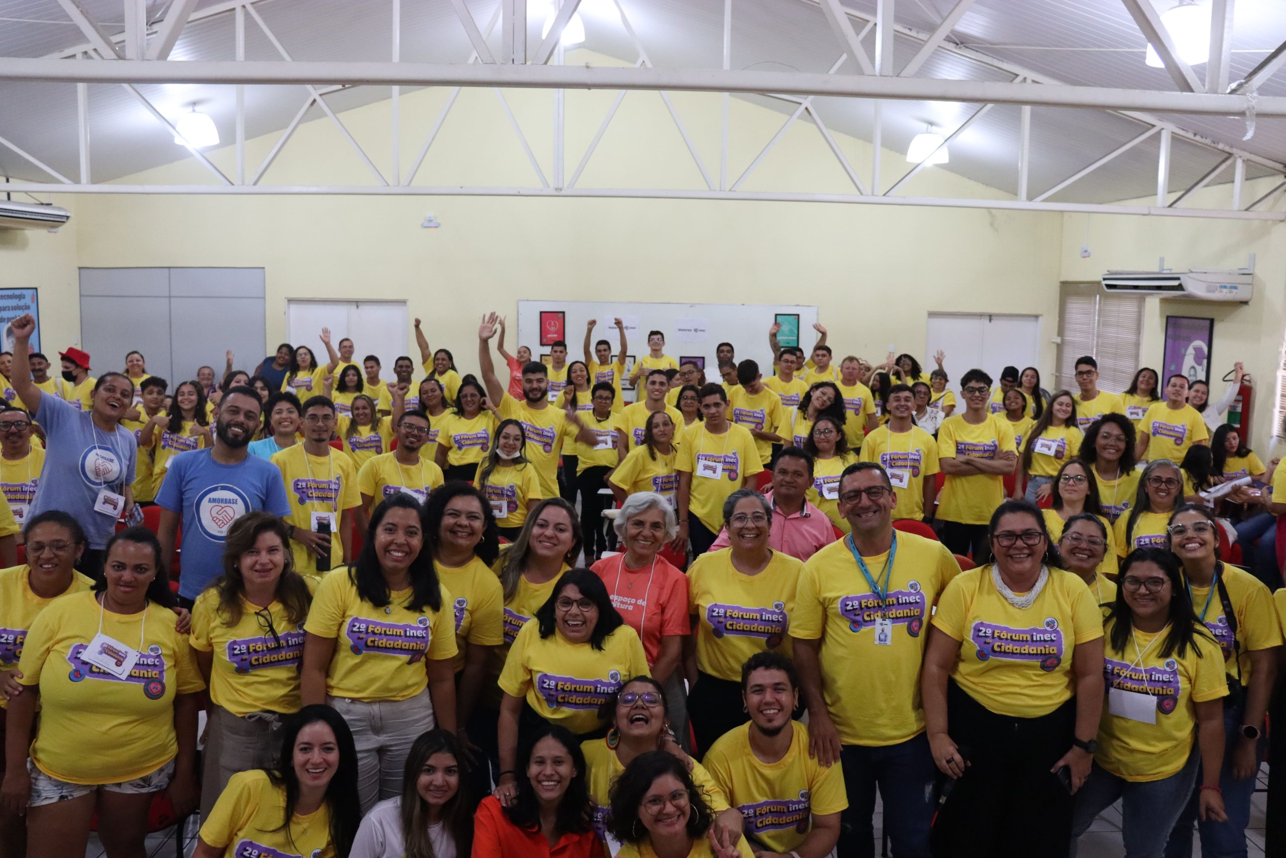 A foto é uma panorâmica no final do II fórum inec de cidadania mostrando todos os participantes vestindo camisa amarela com a identidade visual do evento